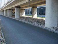 a long concrete highway bridge over a grassy area and sidewalk underneath the bridge with lights on,