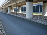 a long concrete highway bridge over a grassy area and sidewalk underneath the bridge with lights on,