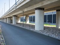 a long concrete highway bridge over a grassy area and sidewalk underneath the bridge with lights on,