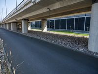 a long concrete highway bridge over a grassy area and sidewalk underneath the bridge with lights on,