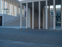 empty street lined with cement buildings next to a tall building with a staircase up to it