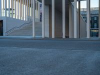 empty street lined with cement buildings next to a tall building with a staircase up to it