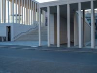 empty street lined with cement buildings next to a tall building with a staircase up to it