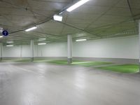 large indoor space with green flooring and concrete ceilinging with two sign posts at the end