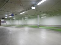 large indoor space with green flooring and concrete ceilinging with two sign posts at the end