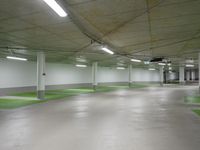 large indoor space with green flooring and concrete ceilinging with two sign posts at the end