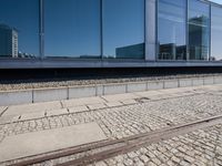 a train track that is next to a large building with glass windows and brick floors