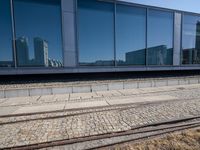 a train track that is next to a large building with glass windows and brick floors