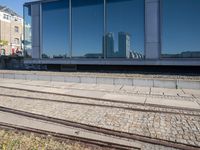 a train track that is next to a large building with glass windows and brick floors