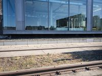 a train track that is next to a large building with glass windows and brick floors