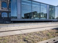 a train track that is next to a large building with glass windows and brick floors