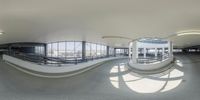 a fish - eye lens panorama shows people walking around the walkway at the airport while the traffic on the way is turning on