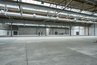 an indoor warehouse area with concrete floors and exposed ceilings, and overhead air vents and metal poles