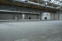 an indoor warehouse area with concrete floors and exposed ceilings, and overhead air vents and metal poles