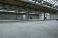 an indoor warehouse area with concrete floors and exposed ceilings, and overhead air vents and metal poles