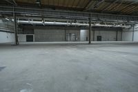 an indoor warehouse area with concrete floors and exposed ceilings, and overhead air vents and metal poles