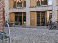 there is a cobbled walk way near the building in the city with parked bicycles