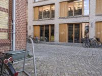 there is a cobbled walk way near the building in the city with parked bicycles