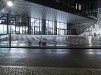 the night time photo shows an empty sidewalk in front of a modern building with many glass doors and windows