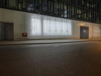 a street at night in front of a big glass building with white sheer drapes