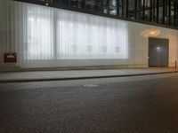 a street at night in front of a big glass building with white sheer drapes