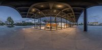 a view of an outdoor bus stop from inside a circular glass door tunnel with a metal roof