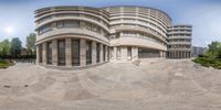 the panoramic view of a circular building and surrounding vegetation is captured from the front