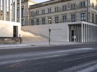 the large, empty sidewalk with multiple columns in front of the building with two signs