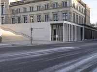 the large, empty sidewalk with multiple columns in front of the building with two signs