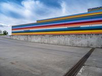 an empty parking lot painted brightly stripes on the wall of the building and sky as well as stones