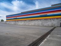 an empty parking lot painted brightly stripes on the wall of the building and sky as well as stones