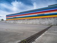 an empty parking lot painted brightly stripes on the wall of the building and sky as well as stones