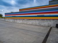 an empty parking lot painted brightly stripes on the wall of the building and sky as well as stones