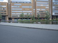 a paved street in front of a tall building and a body of water and trees