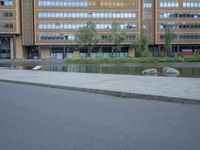 a paved street in front of a tall building and a body of water and trees