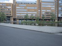 a paved street in front of a tall building and a body of water and trees