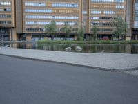 a paved street in front of a tall building and a body of water and trees