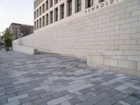 a white building with bricks surrounding it and sidewalk in front of it with stairs leading into