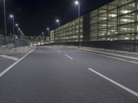 an empty street lined with lights in front of building at night, with a half empty road between two large office buildings