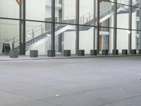 a boy walks on the concrete by some stairs next to a building with many glass walls