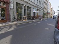 a narrow urban street with cars parked on the side and people walking around the street