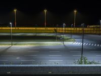 an empty road at night with light posts and lights on both sides of it and an empty field of grass below