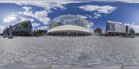 a panoramic shot of a shopping center with a circular mirror pattern and a cloudy sky background