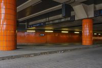 an underpass in a train station with orange tile walls and an empty platform next to the curb