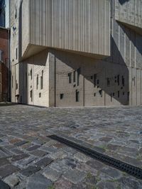 cobblestone driveway surrounded by modern buildings on sunny day with sun reflecting onto the windows