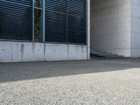the black skateboard is in front of a tall building with lots of windows and concrete