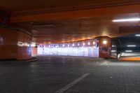 a sidewalk in a tunnel with orange light at the end of it and traffic passing through it