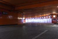 a sidewalk in a tunnel with orange light at the end of it and traffic passing through it