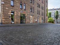 a motorcycle is driving down an empty street in a city corner, with cobblestone street