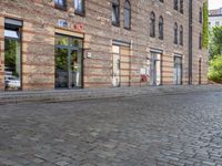 a motorcycle is driving down an empty street in a city corner, with cobblestone street